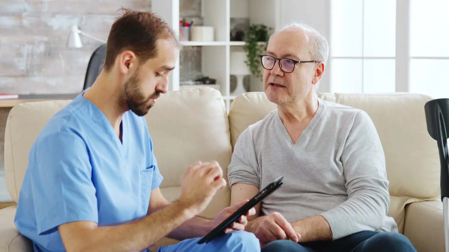 Pflegekraft bespricht mit einem älteren Patienten die Versorgung nach einem Krankenhausaufenthalt zu Hause in Hamburg